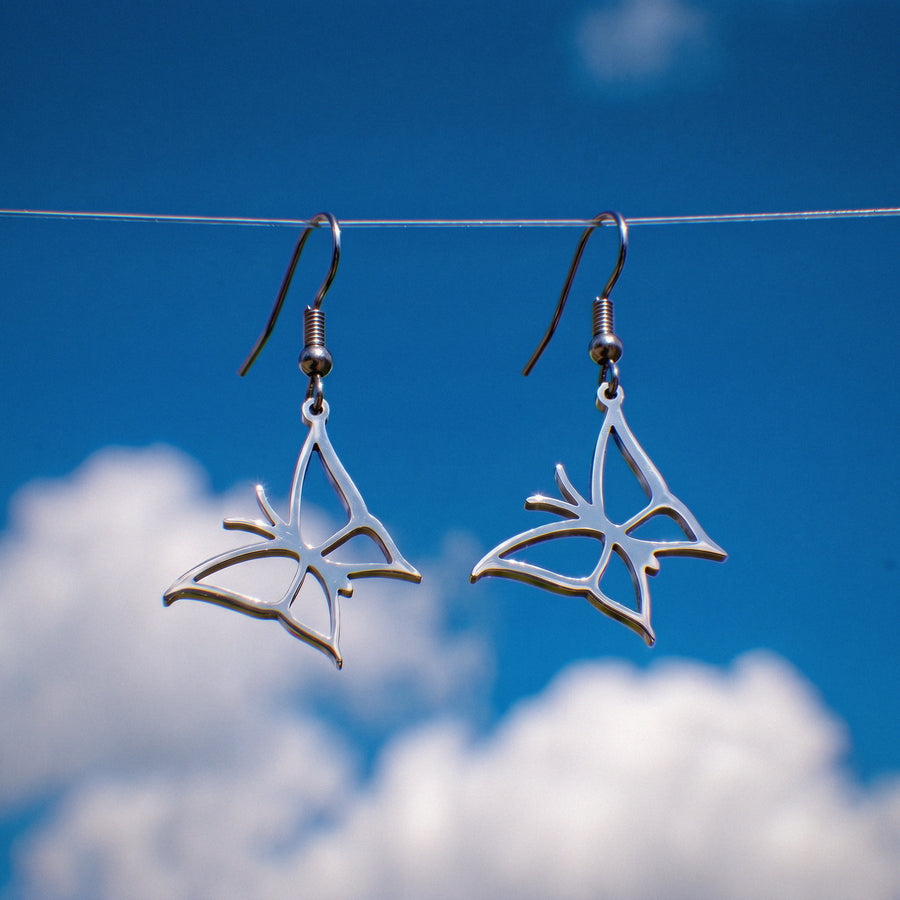 Butterfly earrings in silver stainless steel, hanging against a blue sky